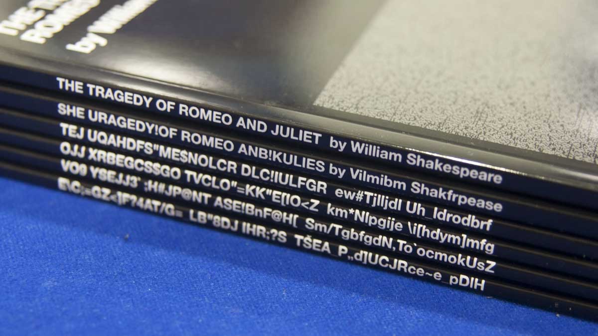 Six books piled up. The spine of the top reads 'The Tragedy of Romeo and Juliet'; the rest are jumbled strings of characters.